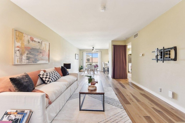 living room with light wood-type flooring, visible vents, ceiling fan, and baseboards