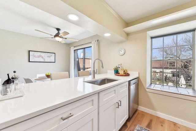 kitchen with light countertops, white cabinetry, a sink, dishwasher, and baseboards