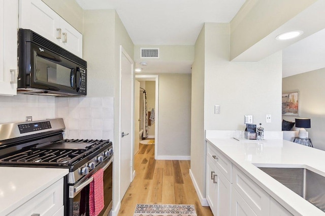 kitchen featuring gas stove, black microwave, visible vents, and white cabinets