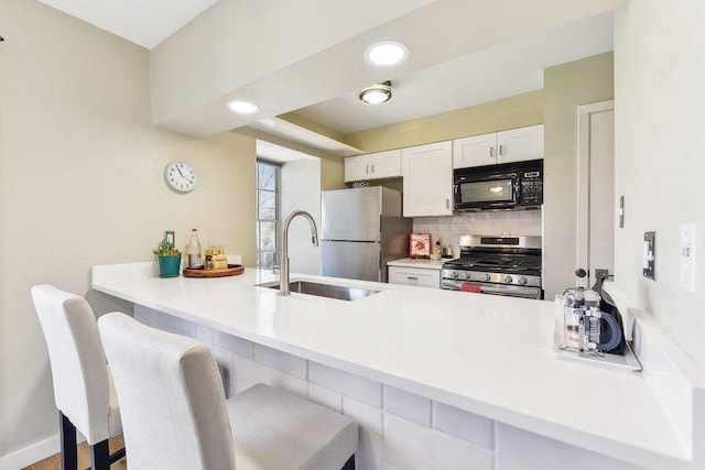 kitchen featuring a breakfast bar area, appliances with stainless steel finishes, white cabinetry, a sink, and a peninsula