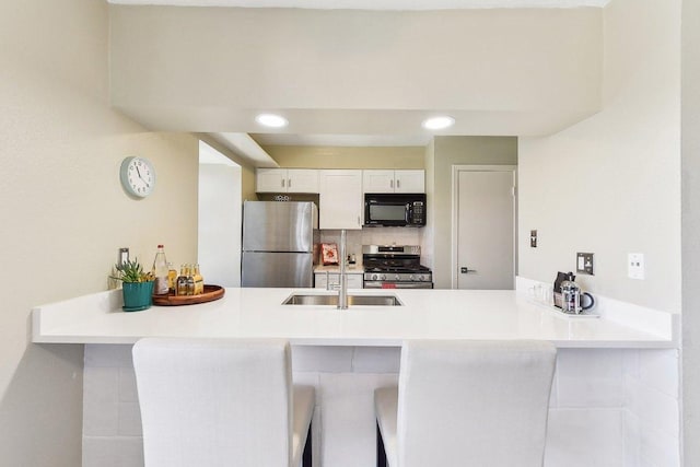 kitchen with a peninsula, a kitchen breakfast bar, white cabinets, light countertops, and appliances with stainless steel finishes