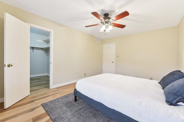 bedroom featuring light wood finished floors, visible vents, baseboards, ceiling fan, and a spacious closet