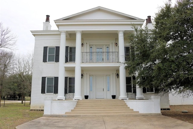 neoclassical home with a balcony, a chimney, and brick siding