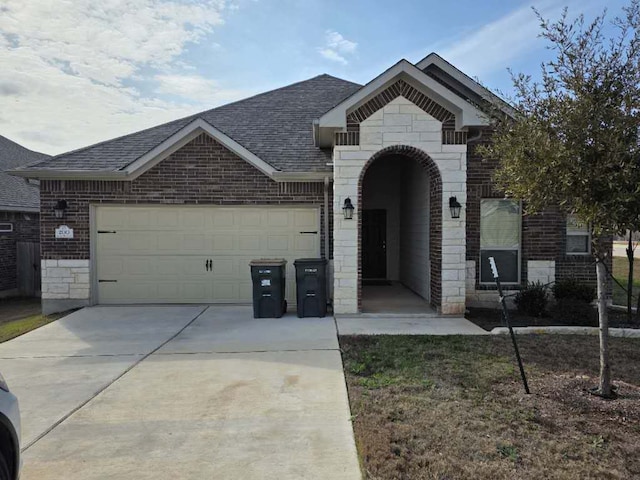 french country style house featuring a shingled roof, stone siding, brick siding, and an attached garage