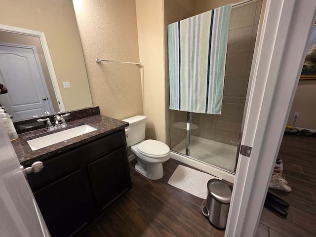 bathroom with a stall shower, a textured wall, toilet, wood finished floors, and vanity