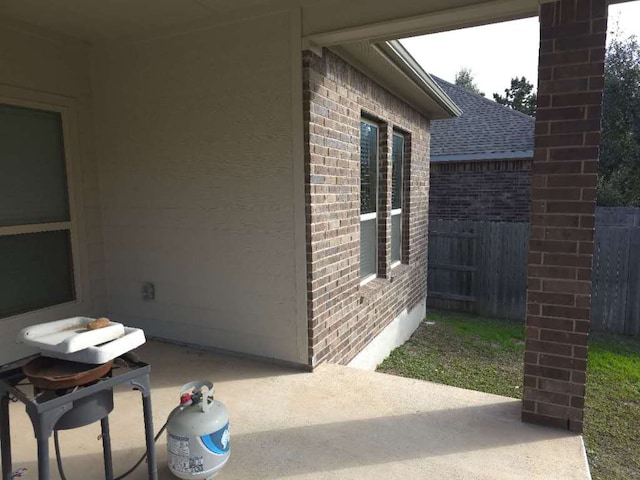 view of side of home featuring a patio, brick siding, a shingled roof, and fence