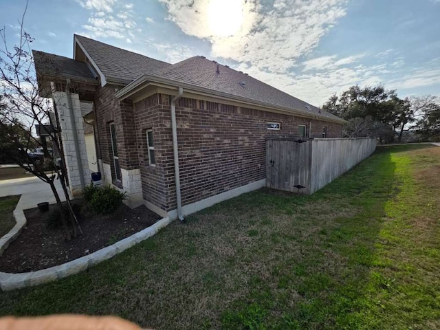 view of side of home featuring roof with shingles, a lawn, and brick siding