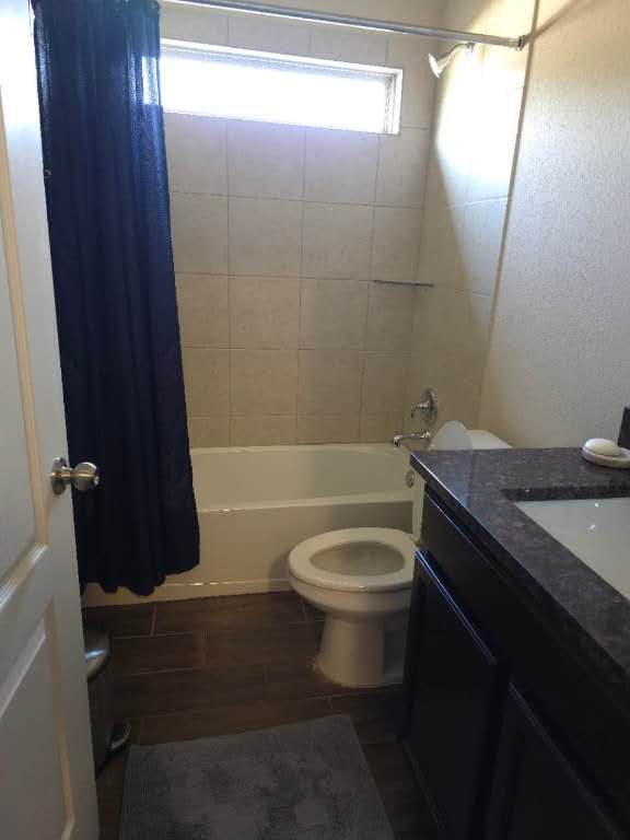 bathroom featuring toilet, shower / bath combo with shower curtain, wood finished floors, and vanity