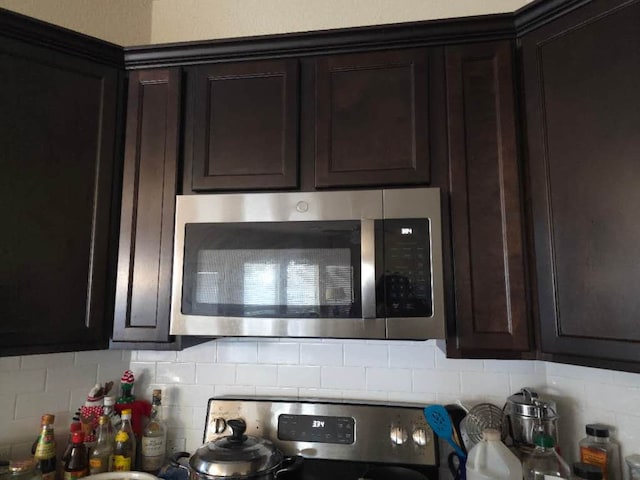 kitchen with stainless steel microwave, decorative backsplash, and dark brown cabinets