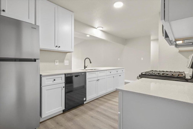 kitchen with black dishwasher, light wood-style floors, freestanding refrigerator, white cabinetry, and a sink