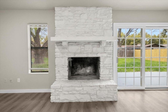 unfurnished living room with a stone fireplace, baseboards, and wood finished floors