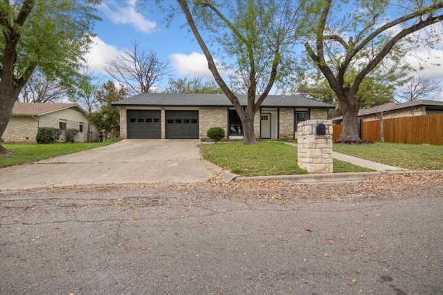 view of front of house with driveway, stone siding, an attached garage, fence, and a front lawn