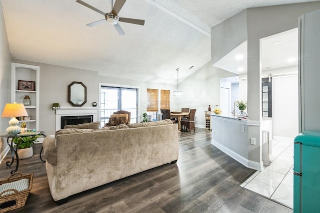 living room featuring lofted ceiling, a textured ceiling, a barn door, a fireplace, and wood finished floors