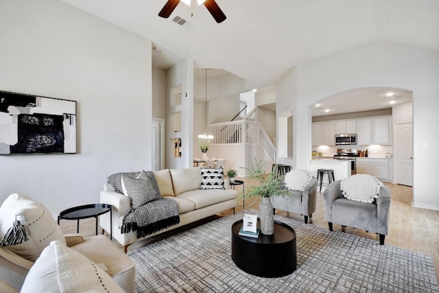 living area featuring light wood finished floors, visible vents, stairway, ceiling fan with notable chandelier, and arched walkways