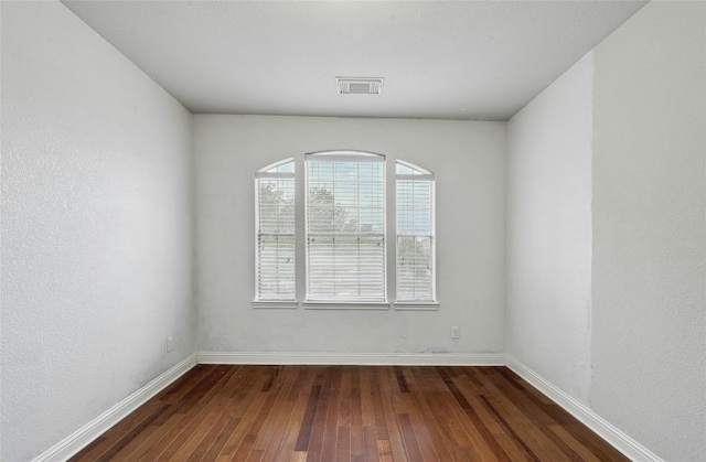 empty room featuring dark wood-style floors, visible vents, and baseboards