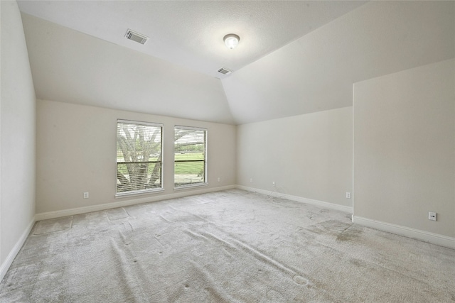 empty room featuring lofted ceiling, light carpet, visible vents, and baseboards