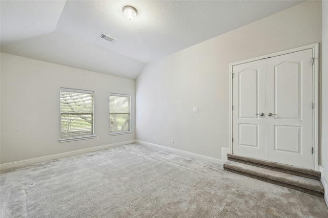 unfurnished room with lofted ceiling, carpet, visible vents, and baseboards