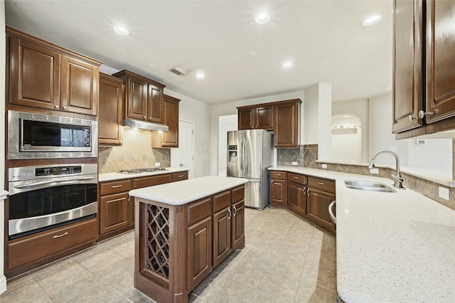 kitchen featuring under cabinet range hood, a kitchen island, a sink, light countertops, and appliances with stainless steel finishes