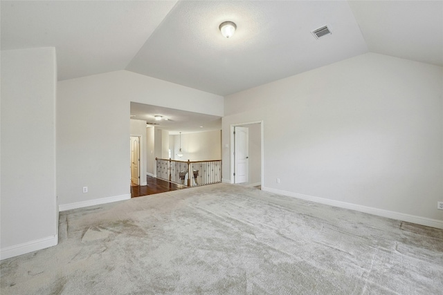 carpeted spare room with lofted ceiling, baseboards, and visible vents