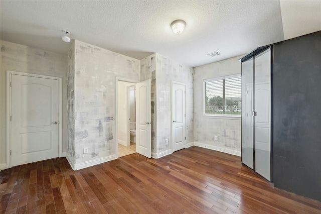 unfurnished bedroom with hardwood / wood-style flooring, baseboards, visible vents, and a textured ceiling