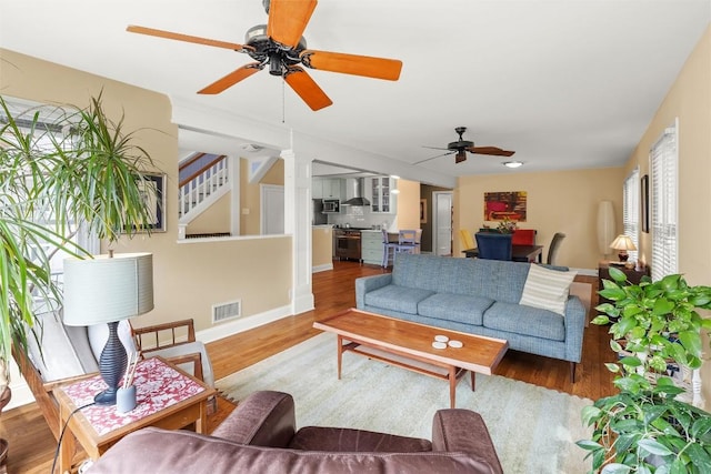 living area featuring wood finished floors, a ceiling fan, visible vents, baseboards, and stairway