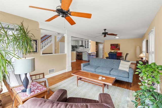 living room featuring baseboards, visible vents, wood finished floors, stairway, and ceiling fan