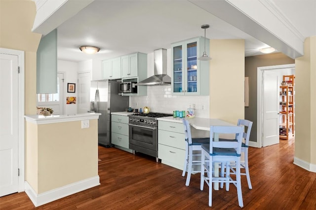 kitchen with dark wood-style floors, decorative backsplash, glass insert cabinets, wall chimney range hood, and appliances with stainless steel finishes