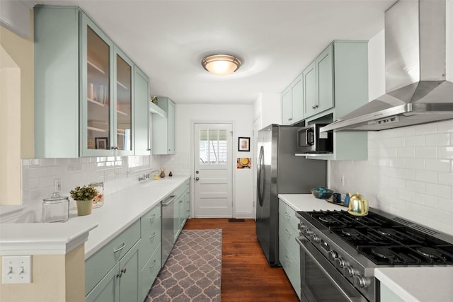 kitchen with dark wood finished floors, stainless steel appliances, light countertops, a sink, and wall chimney range hood