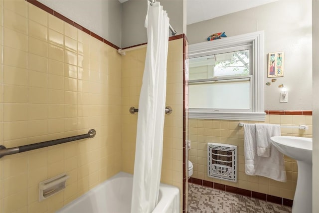 full bath featuring heating unit, shower / bathtub combination with curtain, toilet, tile walls, and wainscoting