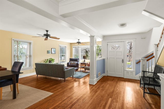 foyer entrance featuring wood finished floors, stairs, ceiling fan, and decorative columns