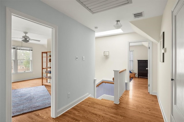 corridor with visible vents, light wood-style flooring, an upstairs landing, and baseboards