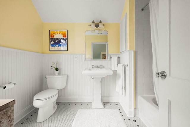 bathroom featuring a wainscoted wall, shower / bathing tub combination, toilet, a sink, and tile patterned flooring