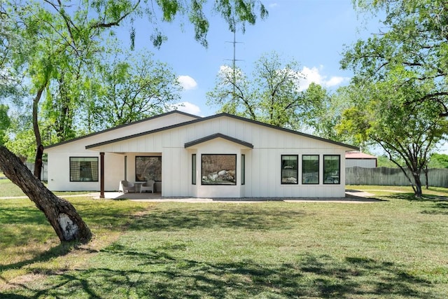 rear view of property featuring a yard, fence, board and batten siding, and a patio