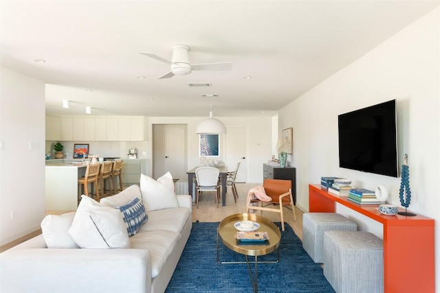 living room featuring a ceiling fan, visible vents, baseboards, and wood finished floors