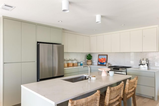 kitchen with a breakfast bar area, a sink, visible vents, appliances with stainless steel finishes, and backsplash