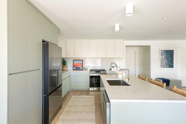 kitchen with a center island with sink, light wood-style flooring, modern cabinets, stainless steel appliances, and a sink