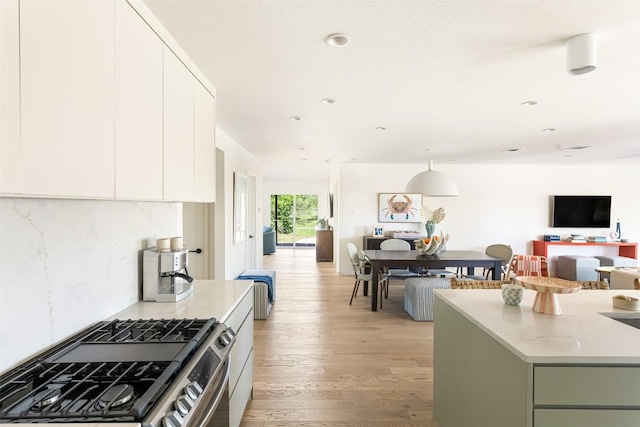 kitchen with tasteful backsplash, gas stove, open floor plan, white cabinets, and light wood-type flooring