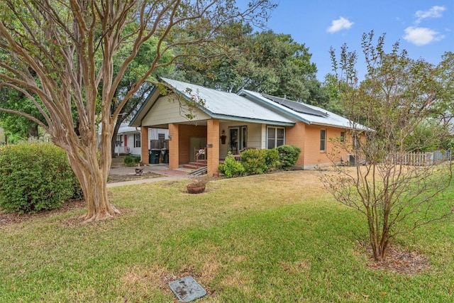 rear view of property with metal roof, an attached carport, a yard, roof mounted solar panels, and brick siding