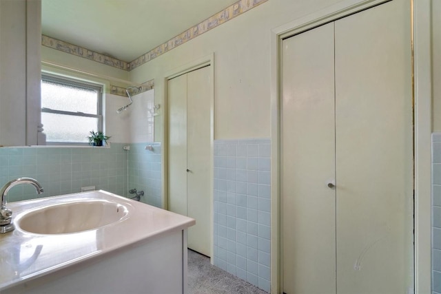 bathroom featuring a shower, wainscoting, vanity, and tile walls