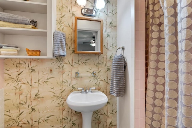 full bath featuring a shower with shower curtain, a sink, and wallpapered walls