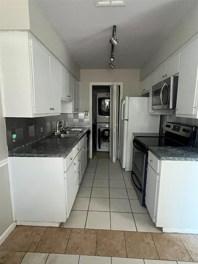 kitchen with stacked washer and clothes dryer, dark countertops, stainless steel appliances, white cabinetry, and a sink