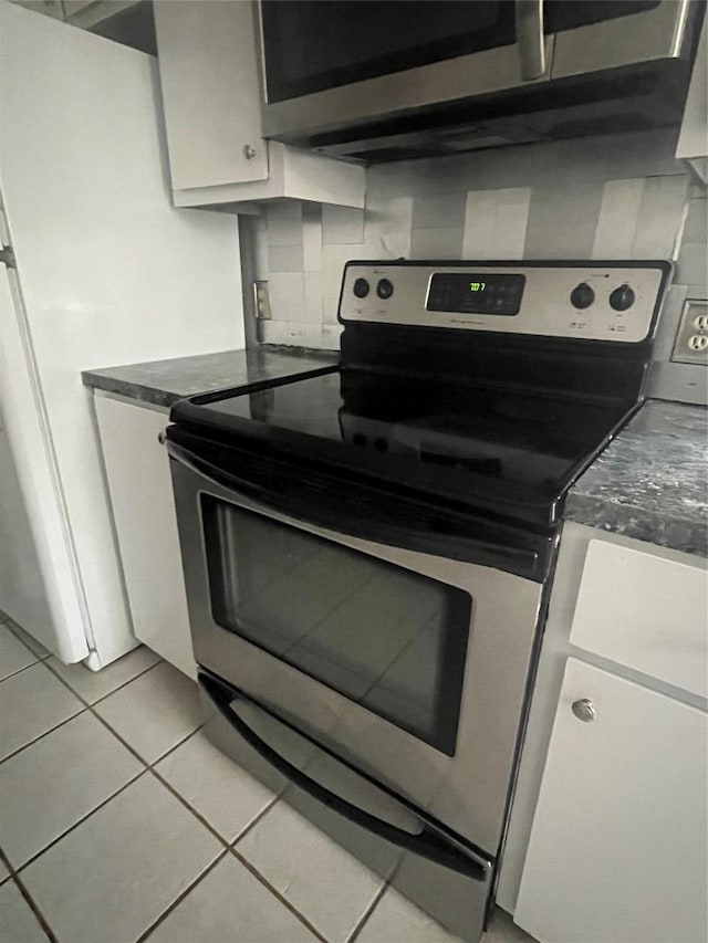 kitchen featuring light tile patterned floors, white cabinetry, appliances with stainless steel finishes, backsplash, and dark countertops