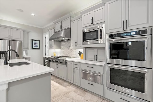 kitchen featuring stainless steel appliances, gray cabinetry, under cabinet range hood, a sink, and a warming drawer