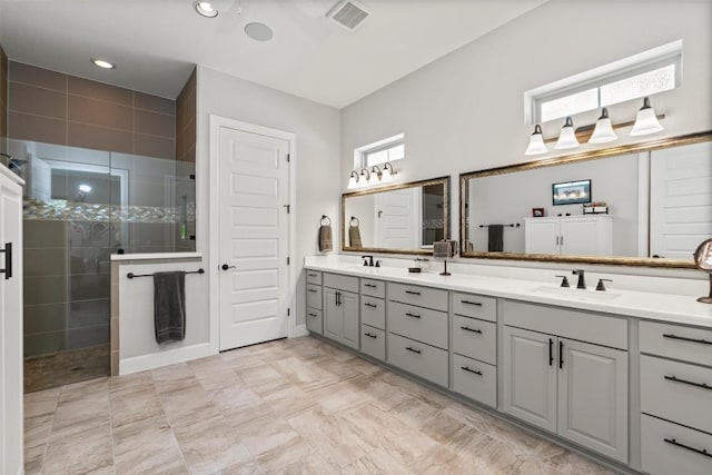 full bath with double vanity, tiled shower, a sink, and visible vents