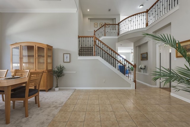 interior space featuring a high ceiling, baseboards, stairs, ornamental molding, and tile patterned floors