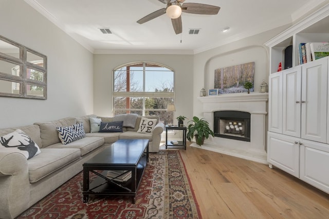 living area with light wood-style flooring, visible vents, and crown molding