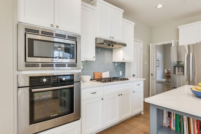 kitchen featuring tasteful backsplash, white cabinets, stainless steel appliances, light countertops, and under cabinet range hood