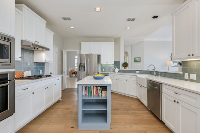 kitchen featuring visible vents, stainless steel appliances, under cabinet range hood, open shelves, and a sink