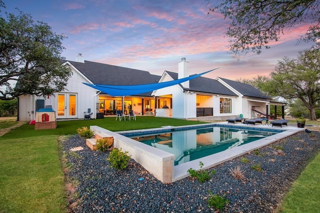 rear view of house with a yard, french doors, board and batten siding, and an outdoor pool