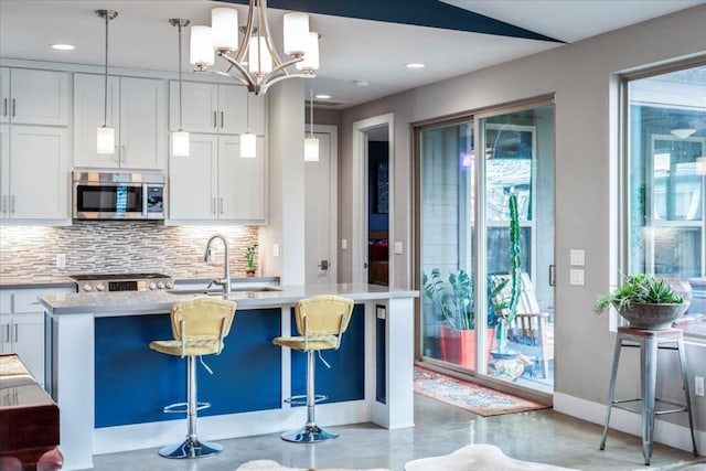 kitchen featuring range, white cabinets, stainless steel microwave, backsplash, and a sink